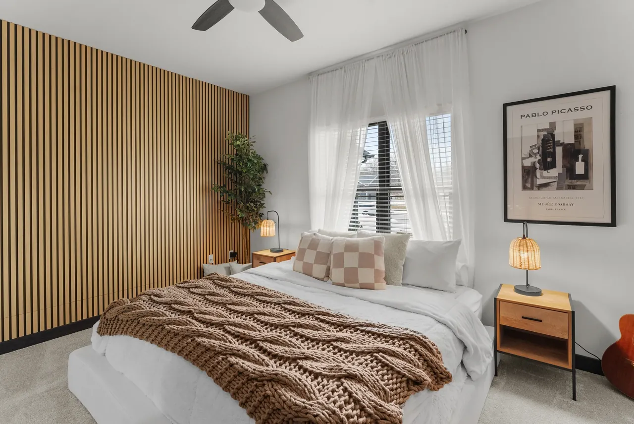 Bedroom with patterned bedding, pendant lighting and a wood accent wall