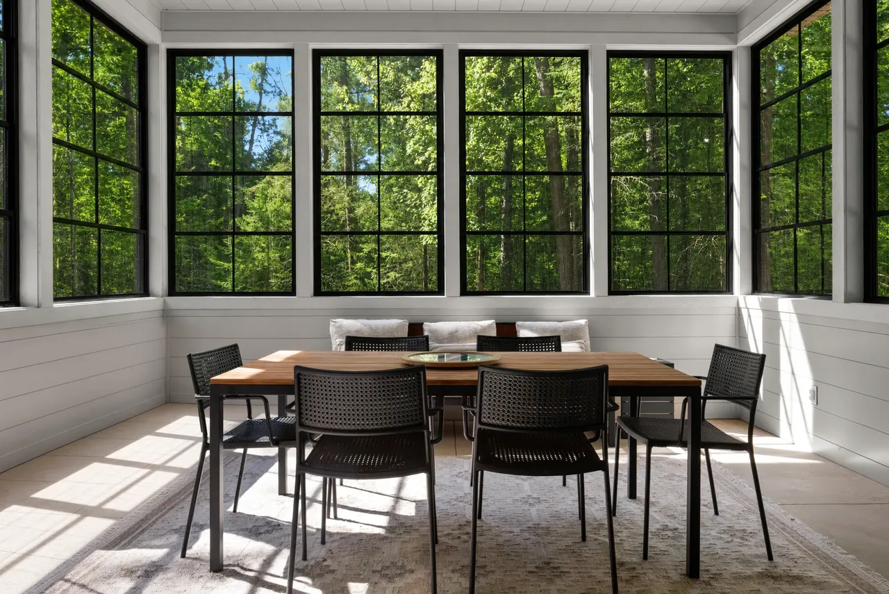 Dining nook with black-framed windows overlooking green trees