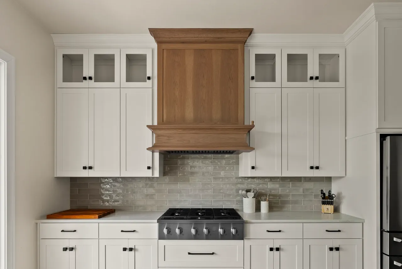 Wood range hood and white cabinetry above a tiled backsplash