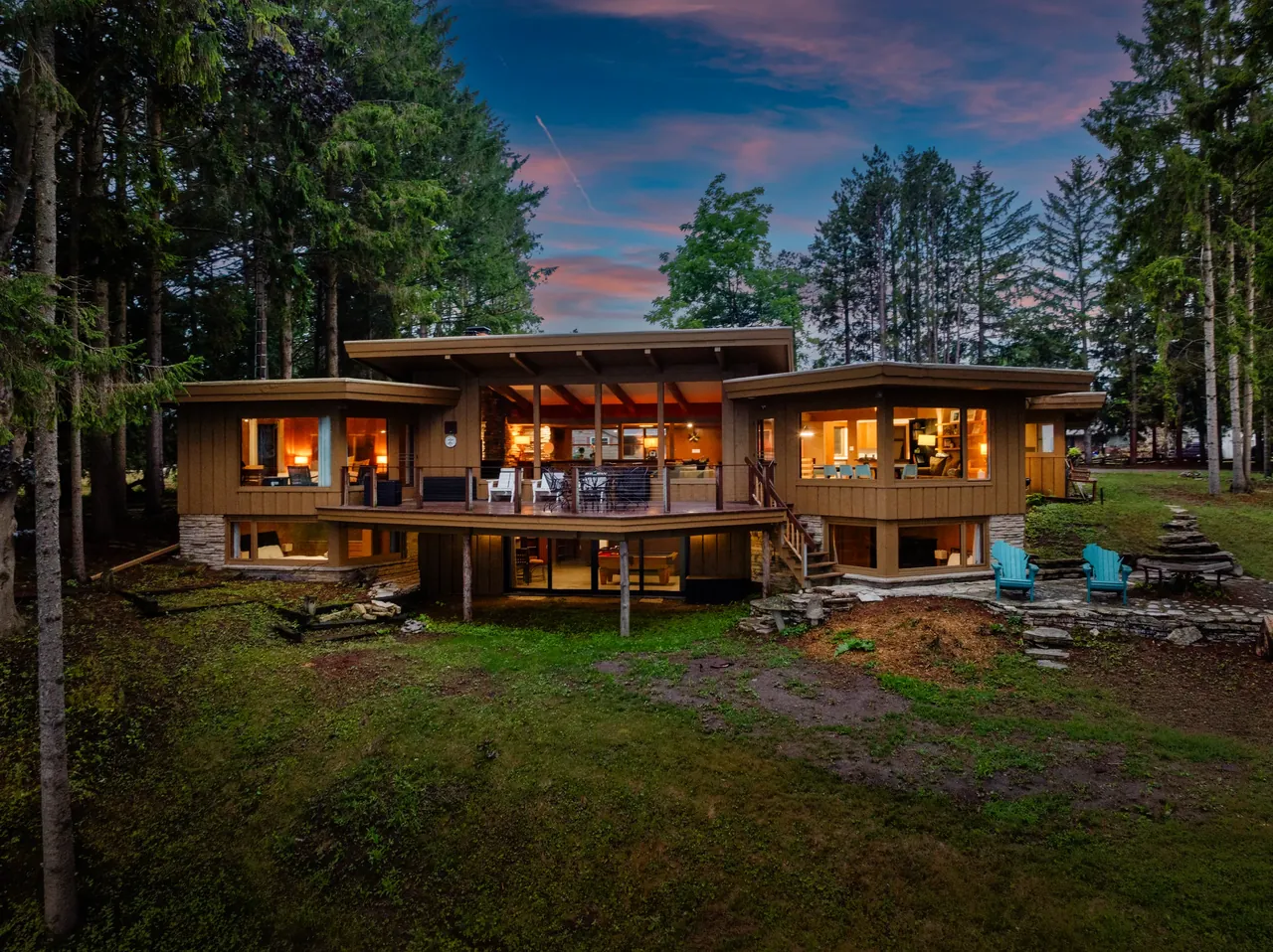 Elevated twilight view of a lit lake house framed by mature trees
