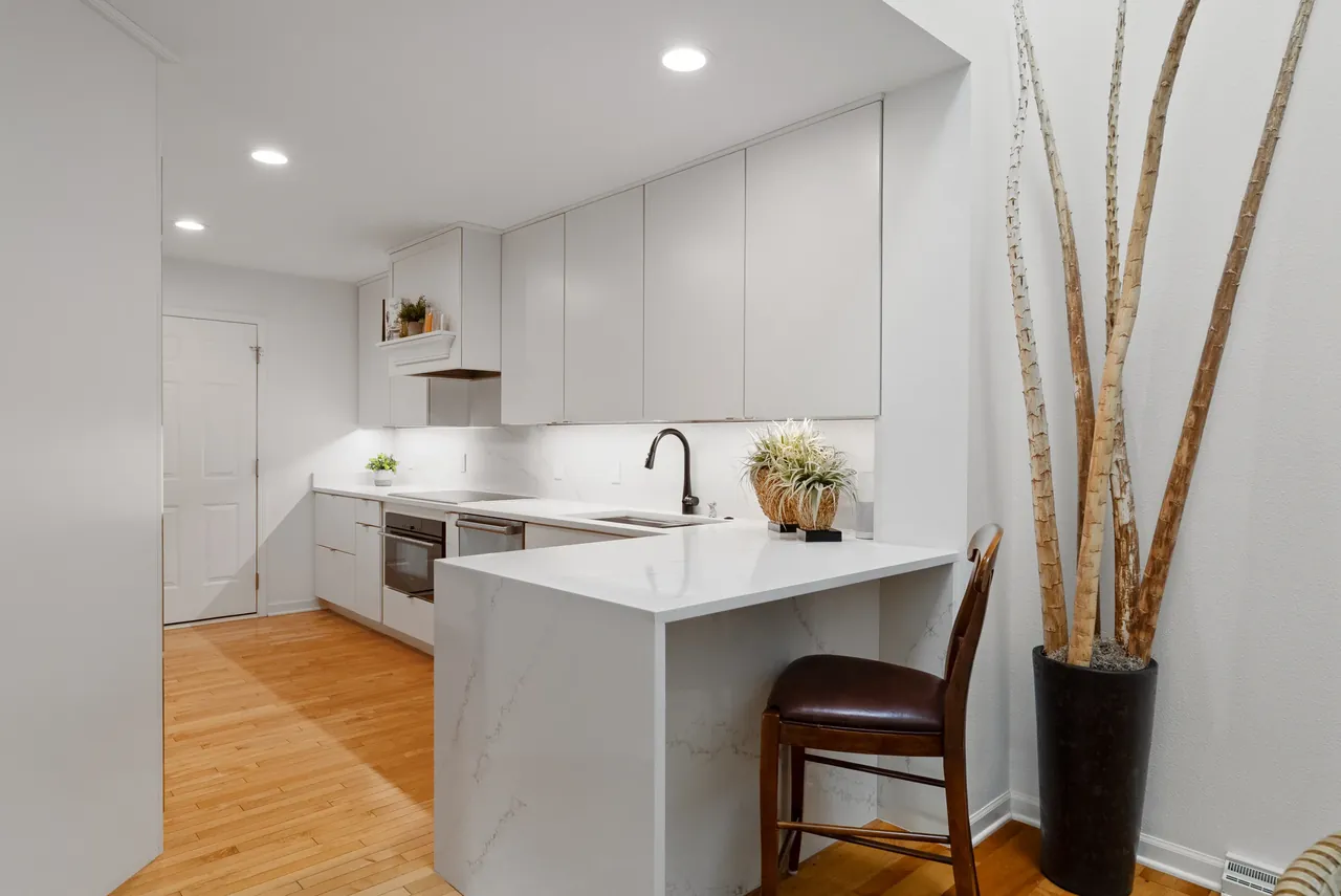 Minimal white kitchen with wood floors and a compact island