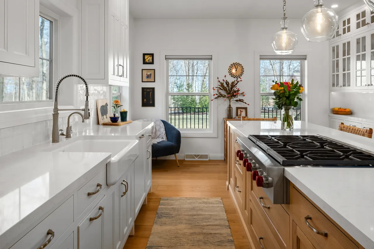 White kitchen with a wide island, wood floor and stainless steel range